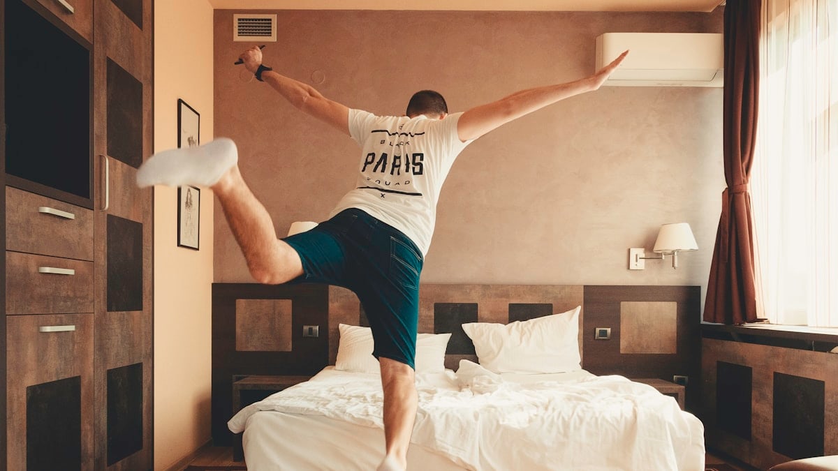 man wearing white shirt about to jump on bed